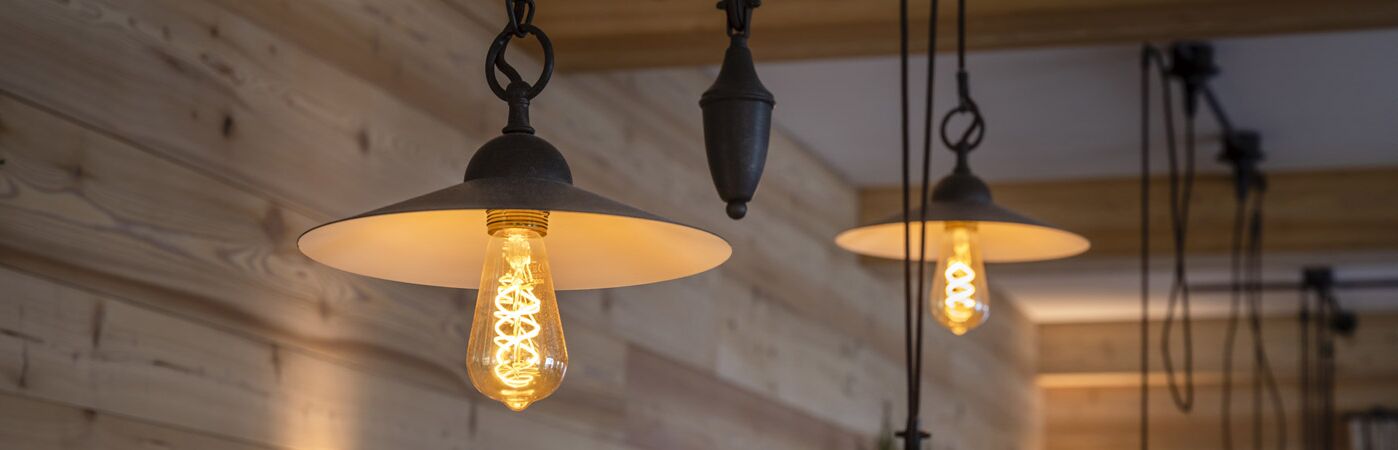 Restaurant Broesel Alm im Berghotel Sudelfeld Blick auf eine Holzwand aus Altholz im Vordergrund verschiedene Designer-Deckenleuchten 